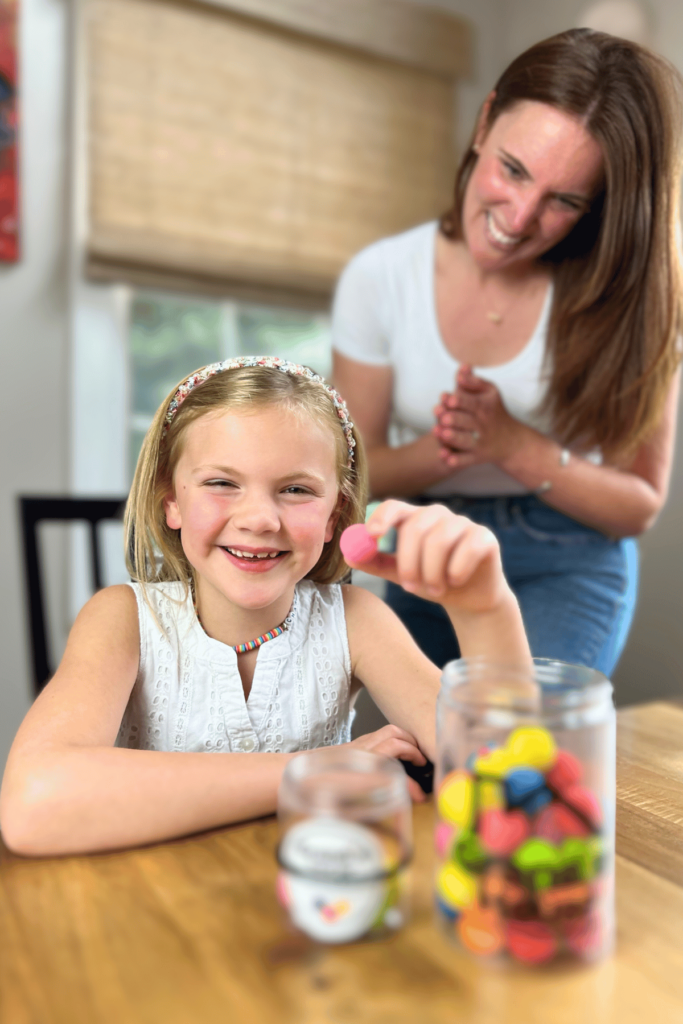 Girl showing her earned Grandie to the camera while her mom proudly smiles behind her